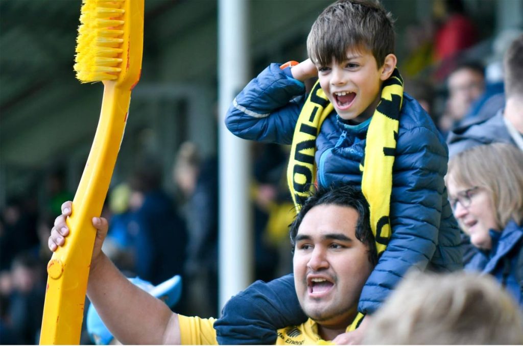 Aficionado del Bodø/Glimt sosteniendo un cepillo de dientes gigante amarillo en la grada.